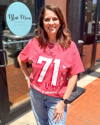 Model wearing a cardinal Arkansas Razorbacks graphic t-shirt with distressed 71 jersey design, Woo Pig lettering, and University of Arkansas graphic.