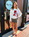 Woman wearing a white sweatshirt with a red graphic design, standing outside a store named 'Blue Moon'.