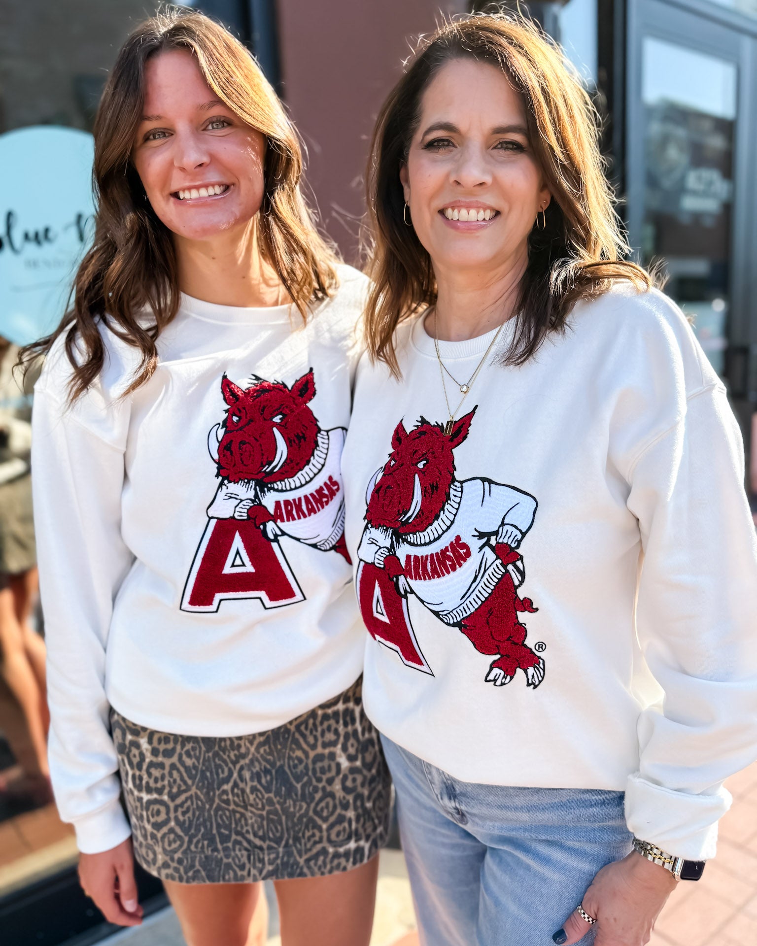 Two women wearing white sweatshirts with red graphics and 'Arkansas' text.