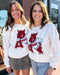 Two women wearing white sweatshirts with red graphics and 'Arkansas' text.