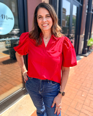 Woman wearing a vibrant red bubble sleeve blouse with a split V-neckline styled with dark denim jeans.