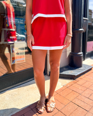 Model wearing a red mini skirt with white contrast trim, styled as part of a matching red and white knit set.