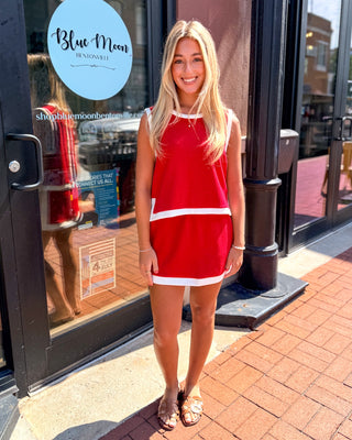 Model wearing a red sleeveless knit tank with white contrast trim and button-back detail.
