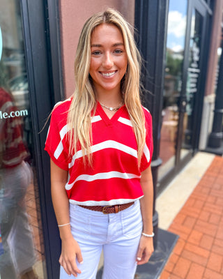 Model wearing a red and white striped short sleeve sweater top with a split V-neckline and relaxed fit paired with white pants.