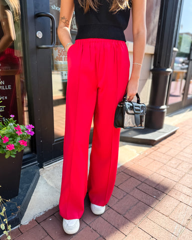 Person wearing red pants and a black top standing on a sidewalk.