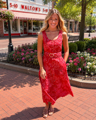 Woman in a red dress standing in front of a store with a floral garden.