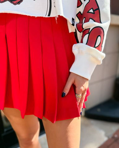 Person wearing a white sweatshirt with red text and a red pleated skirt.