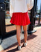 Person wearing a red pleated skirt and white sneakers on a sidewalk.