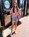 Woman standing outside a store with a red and white striped shirt, denim shorts, and white sneakers.