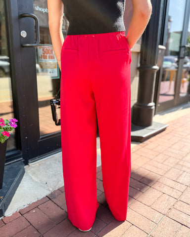 Person wearing red pants standing on a sidewalk with a store entrance in the background
