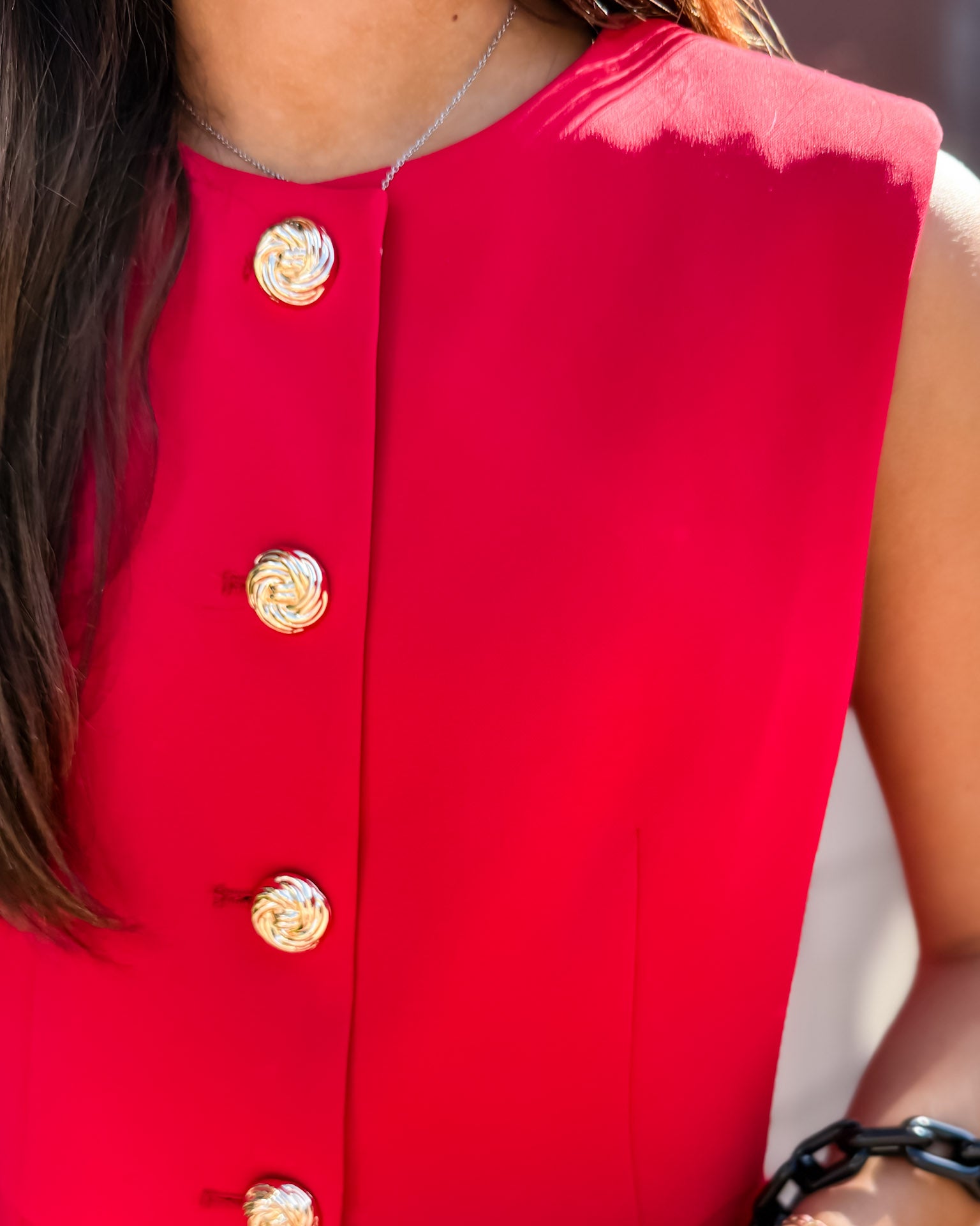 Red sleeveless top with gold buttons worn by a person.