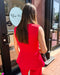 Woman in a red outfit standing outside a building with a sign that reads 'Blue M'.