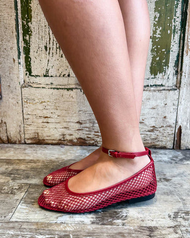 Red mesh flats worn by a person standing on a wooden floor with a rustic background.