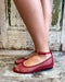 Red mesh flats worn by a person standing on a wooden floor with a rustic background.