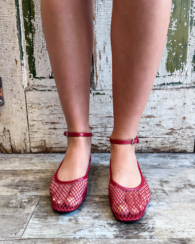 Red mesh shoes worn by a person standing on a wooden floor with a rustic background.