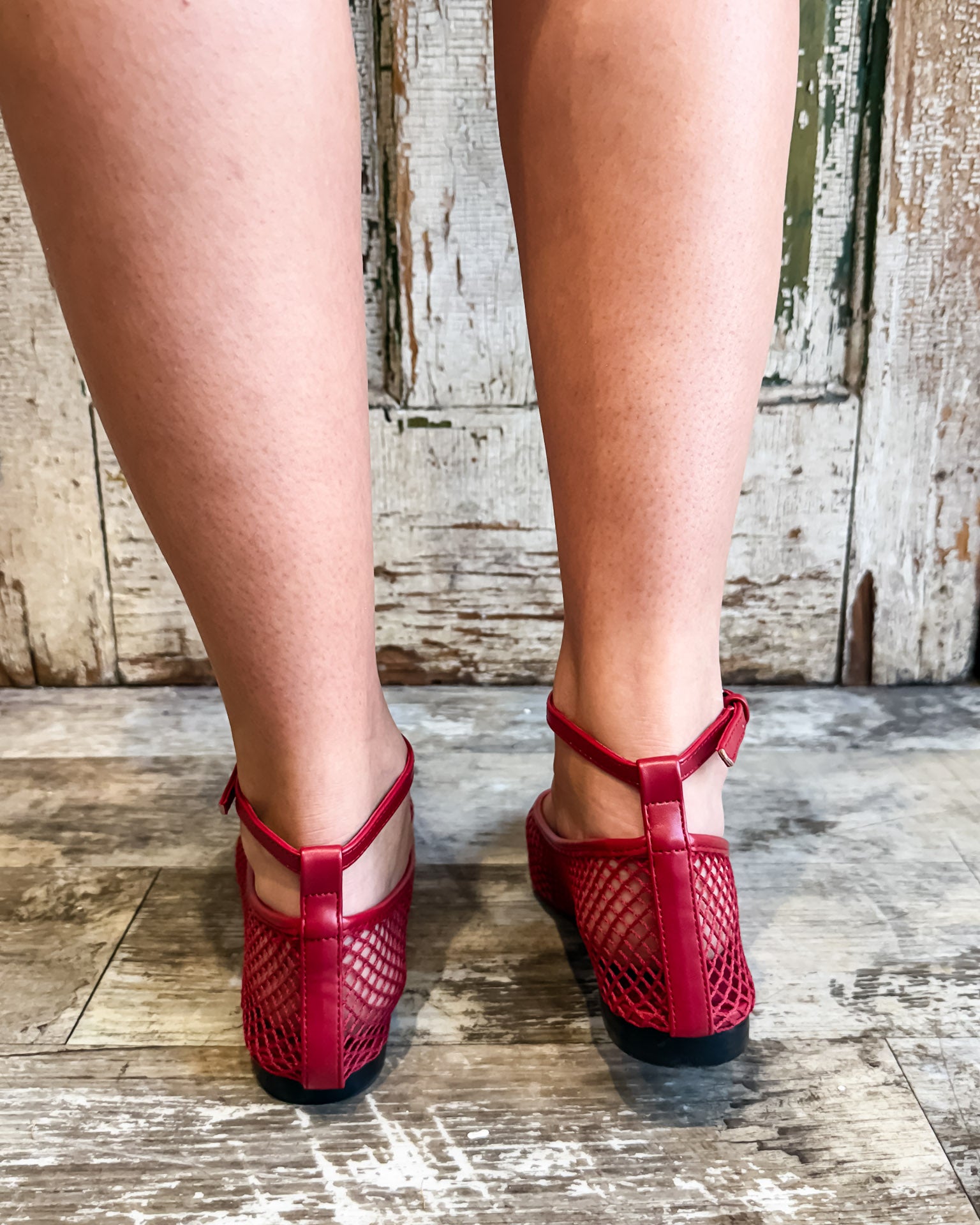 Red open-toe shoes worn on a wooden floor with a rustic background