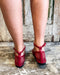 Red open-toe shoes worn on a wooden floor with a rustic background