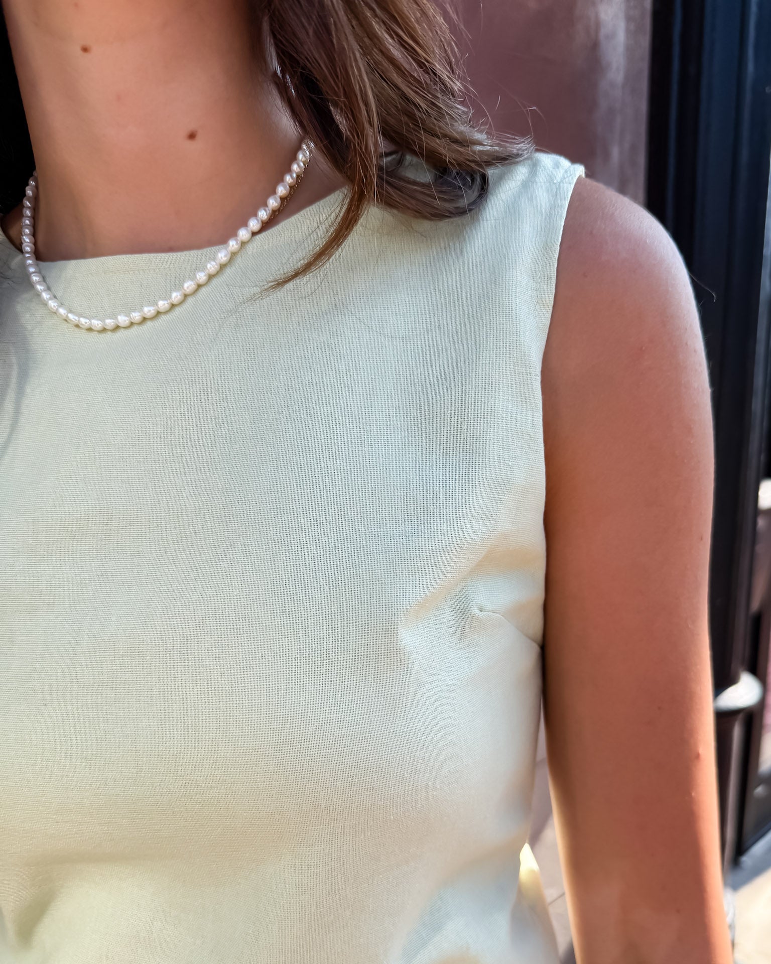 Person wearing a light-colored sleeveless top with a pearl necklace.