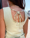 Woman wearing a light-colored sleeveless top with tied back design on a street.
