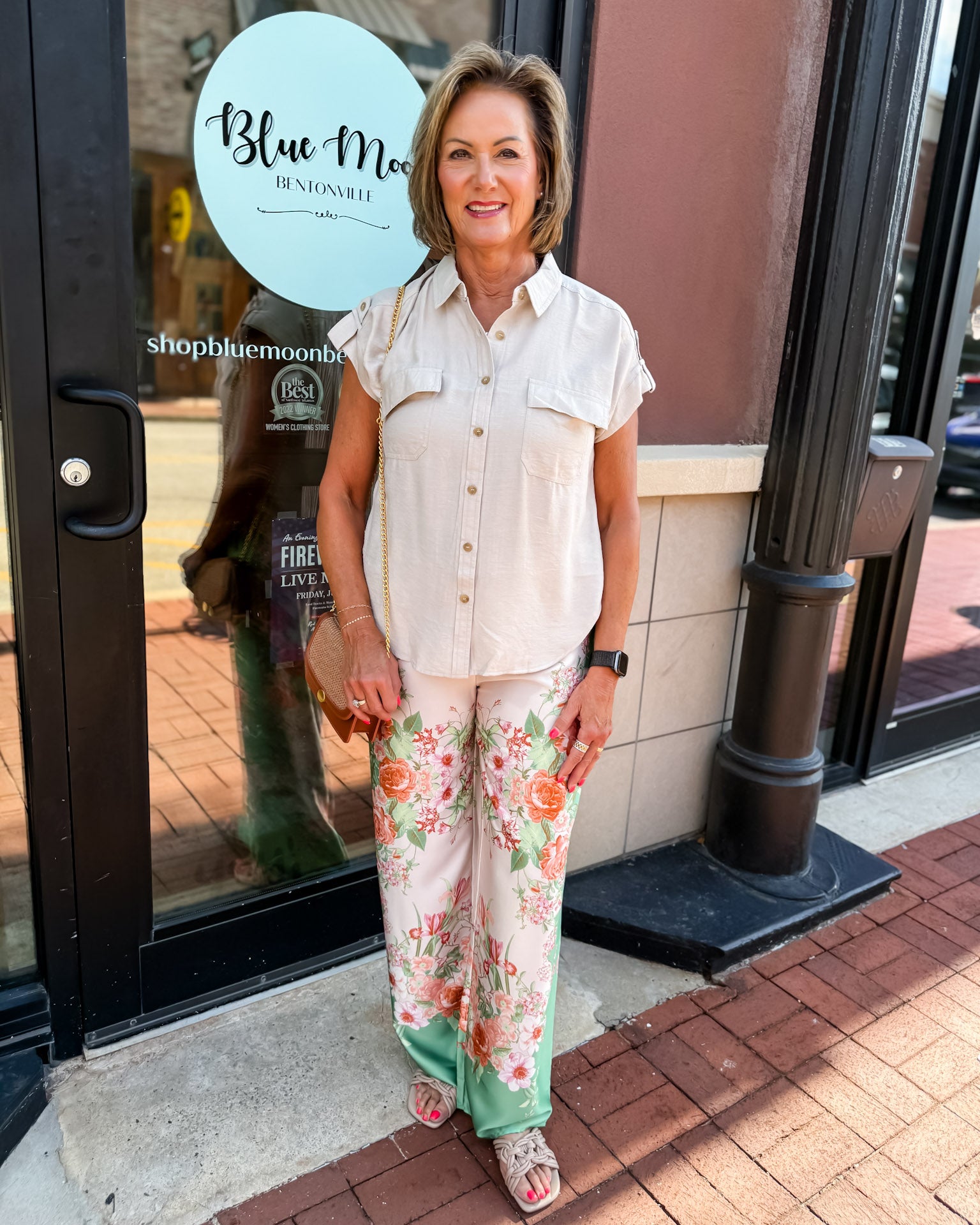 Woman in a light-colored outfit with floral pants standing outside a store named 'Blue Moon'.