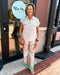 Woman in a light-colored outfit with floral pants standing outside a store named 'Blue Moon'.