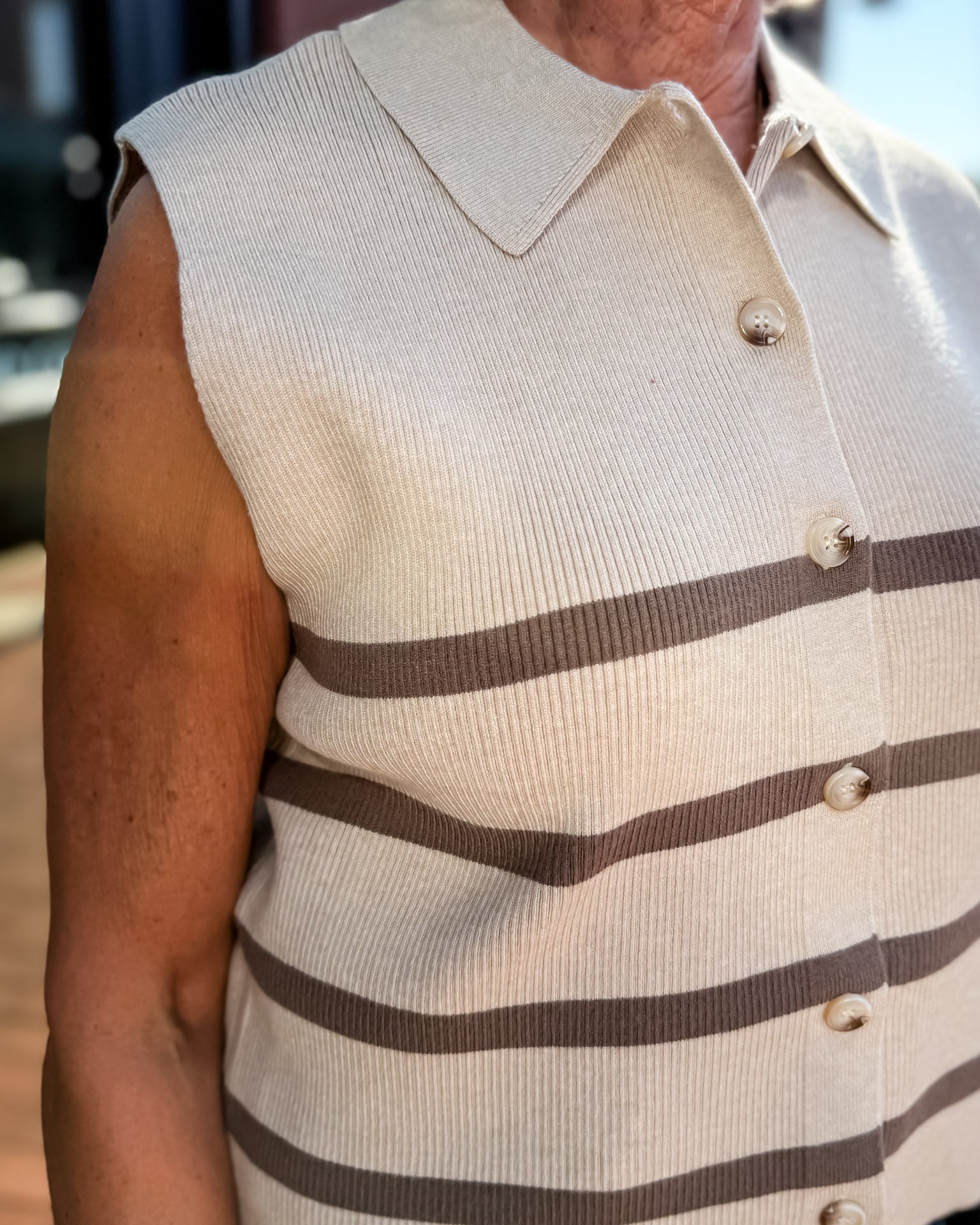 Man wearing a beige sweater vest with brown stripes and a buttoned shirt underneath.
