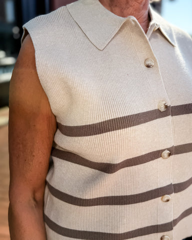 Man wearing a beige sweater vest with brown stripes and a buttoned shirt underneath.