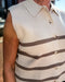 Man wearing a beige sweater vest with brown stripes and a buttoned shirt underneath.