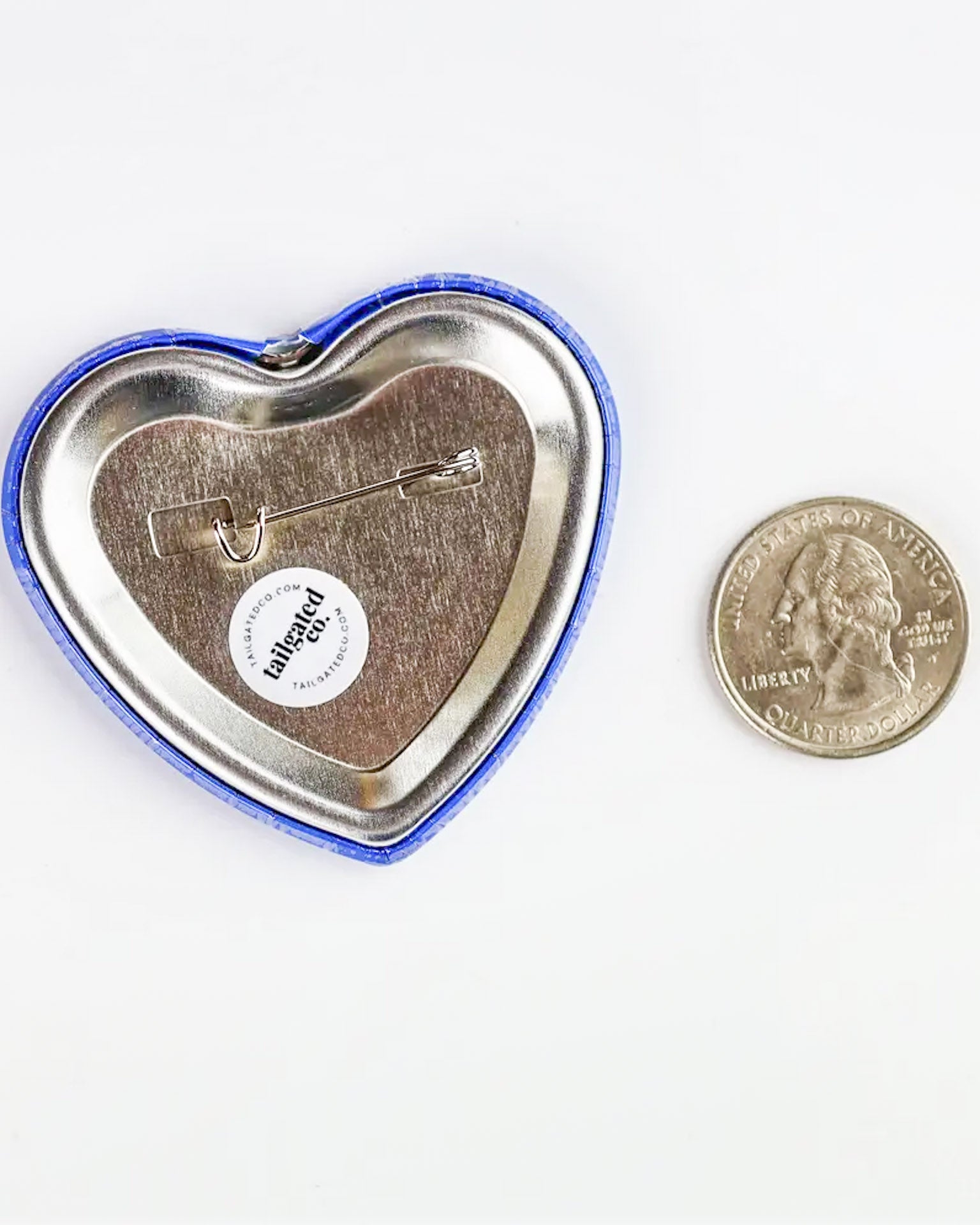 Heart-shaped button badge with a pin on a white background, next to a U.S. quarter for scale.