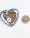 Heart-shaped button badge with a pin on a white background, next to a U.S. quarter for scale.