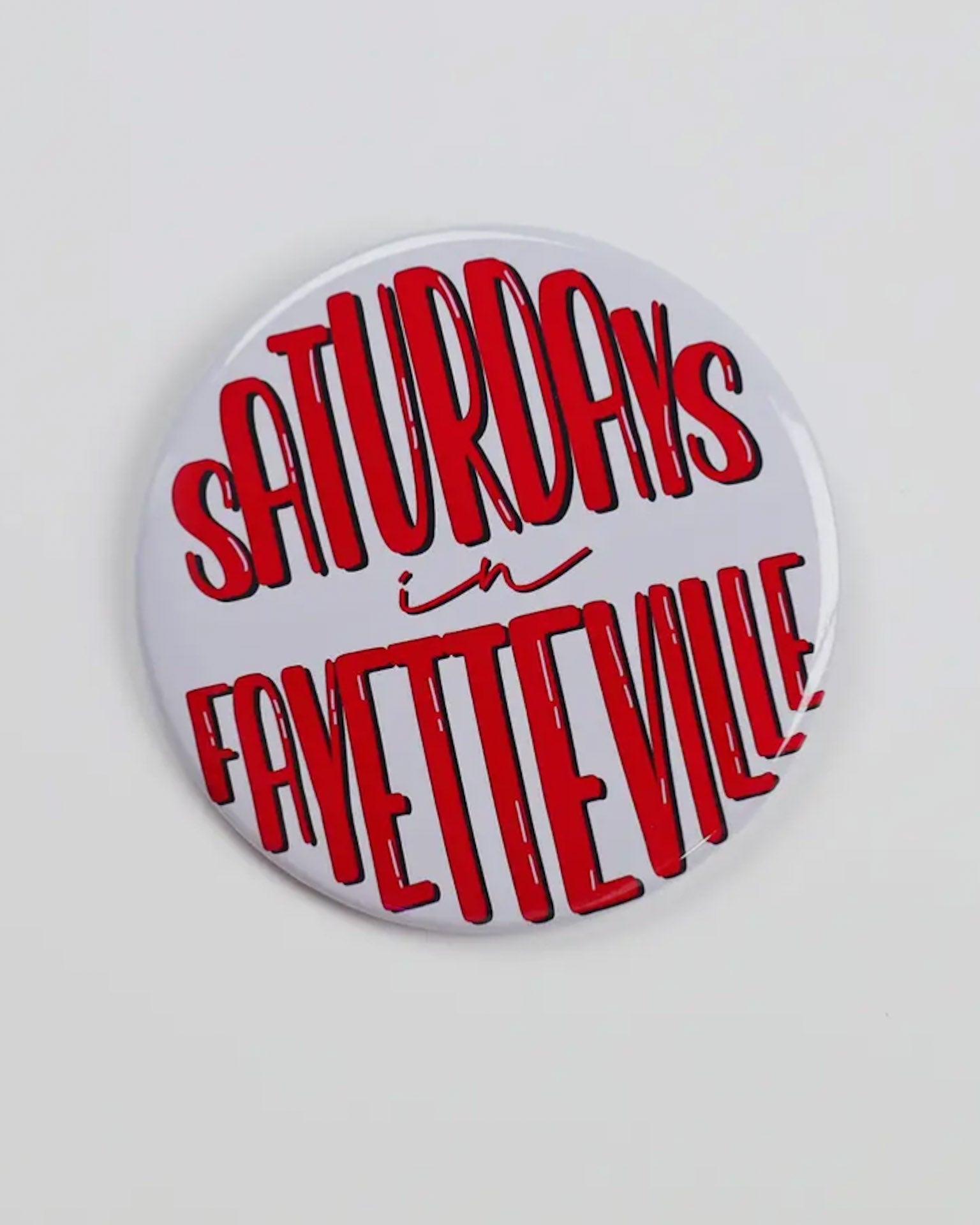 Button badge with 'Saturdays in Fayetteville' text in red on a white background