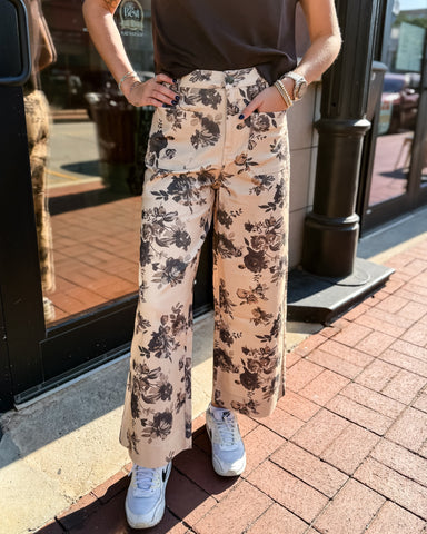Person wearing floral pants and white sneakers on a sidewalk.