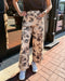 Person wearing floral pants and white sneakers on a sidewalk.
