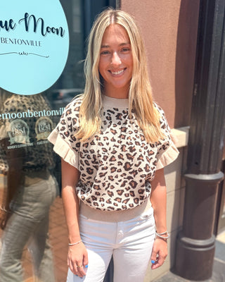 Model wearing a taupe leopard print lightweight sweater with short ruffle sleeves, a crew neckline, and ribbed trim paired with white jeans.