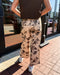 Person wearing floral pants and a dark top standing on a sidewalk.