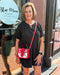 Woman holding a red handbag in front of a store with 'Blue Moon Bentonville' branding.