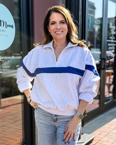 Woman wearing a white sweatshirt with blue stripes and jeans standing in front of a store.