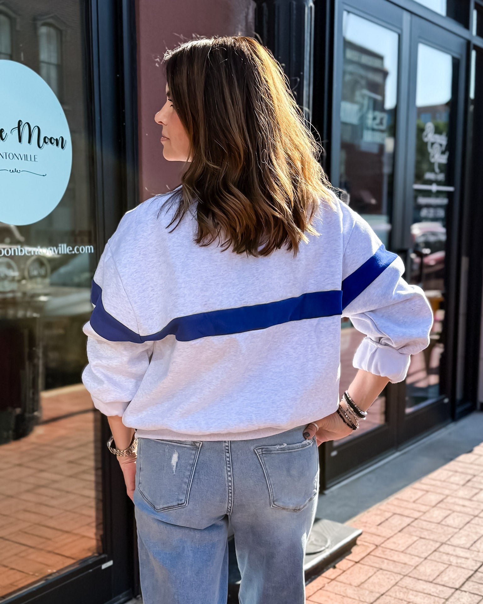 Person wearing a white sweatshirt with blue stripes and jeans standing outside a building.
