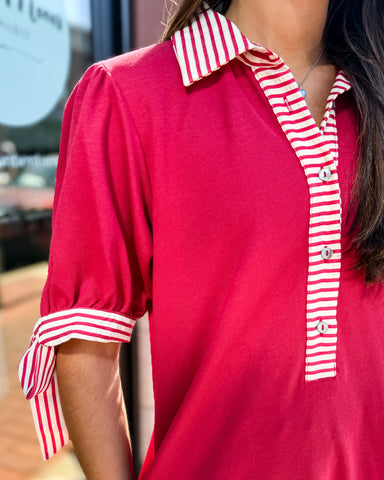 Red shirt with white striped collar and cuffs worn by a person.
