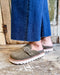 Person wearing olive green suede shoes with white soles on a wooden floor.