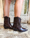 Brown cowboy boots worn by a person on a wooden floor with a rustic background